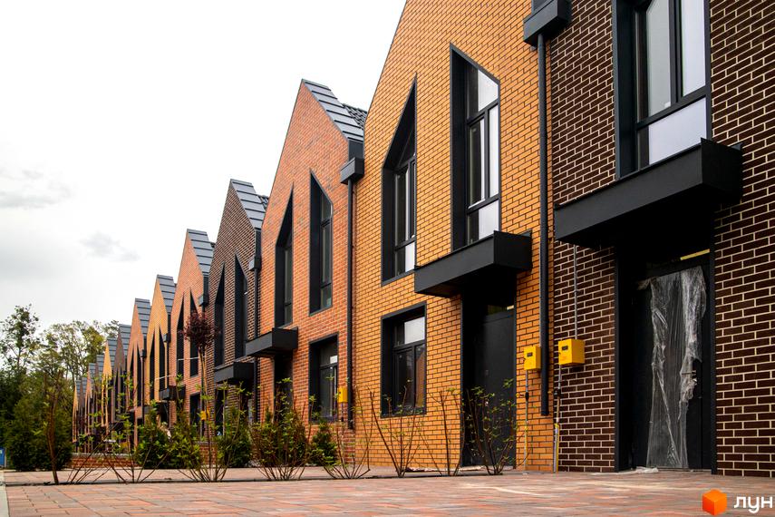Зовнішній вигляд таунхаусів FORT HOMES з цегли з чорними вікнами та дахами. На передньому плані висаджені кущі вздовж тротуару.