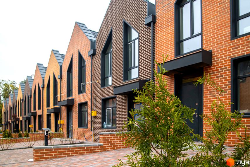 Зовнішній вигляд таунхаусів FORT HOMES з цегли різних кольорів. На передньому плані зелені насадження та викладена бруківкою територія.