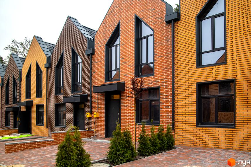 Таунхауси FORT HOMES з цегляним фасадом та незвичними вікнами на тлі сірого неба. Перед будинками викладена бруківка та посаджені туї.