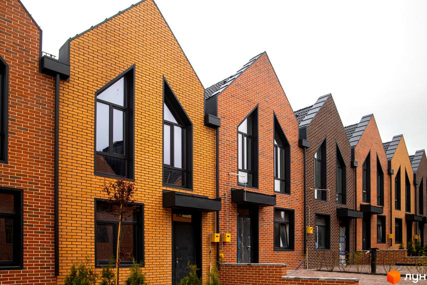 Зображення фасаду таунхаусів FORT HOMES з цегли. На передньому плані видно невеликі дерева та кущі.