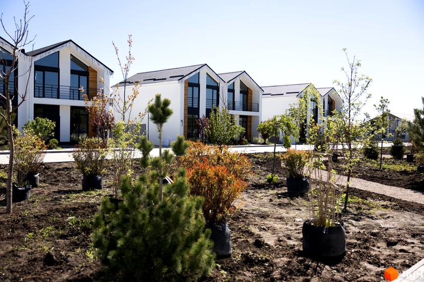 Котеджне містечко Gardd House Eco Village: Ряд білих двоповерхових будинків з темними дахами та великими вікнами. Прибудинкова територія з молодими деревами та кущами.