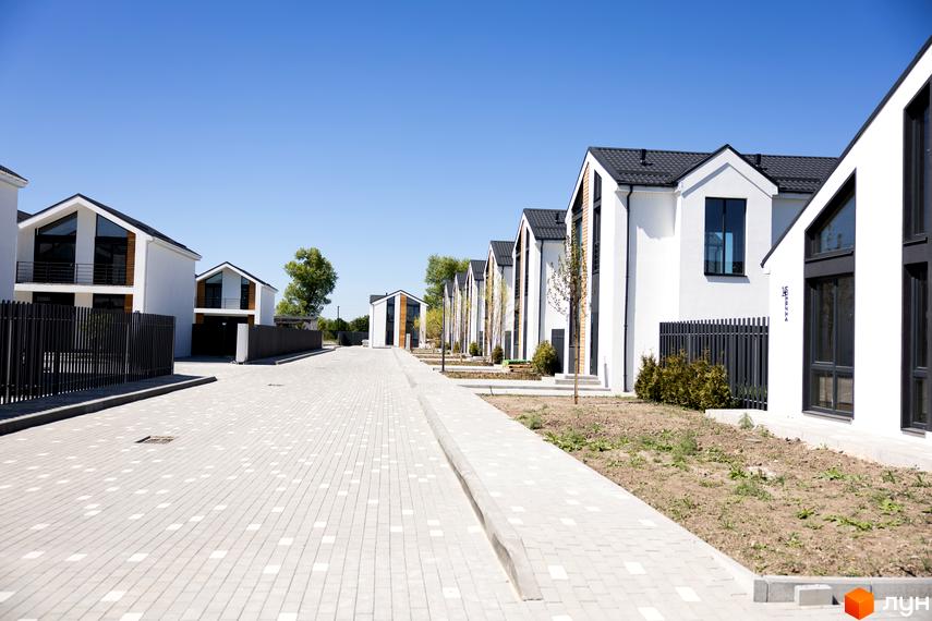 Котеджне містечко Gardd House Eco Village. Ряд білих котеджів з темними дахами та великими вікнами вздовж брукованої дороги.