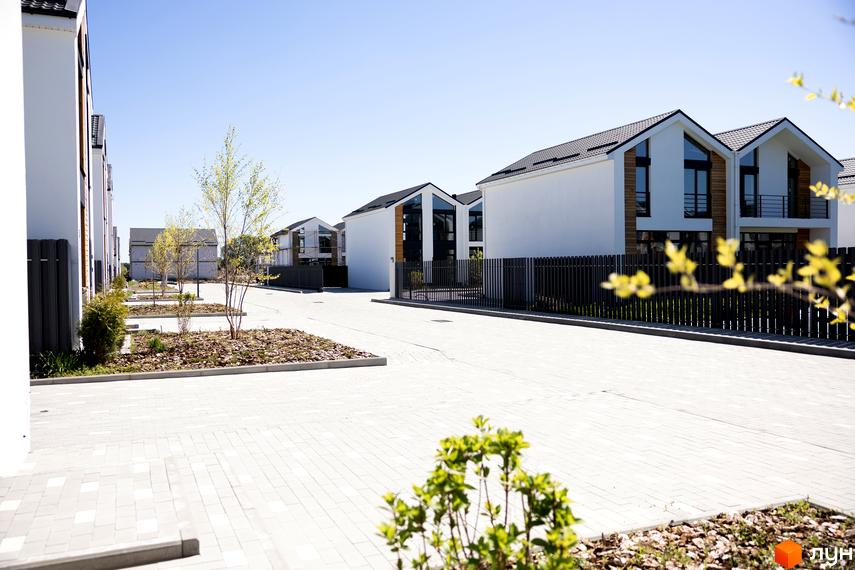 Котеджне містечко Gardd House Eco Village: білі будинки з темними дахами та великими вікнами, бруківка та молоді дерева на території.