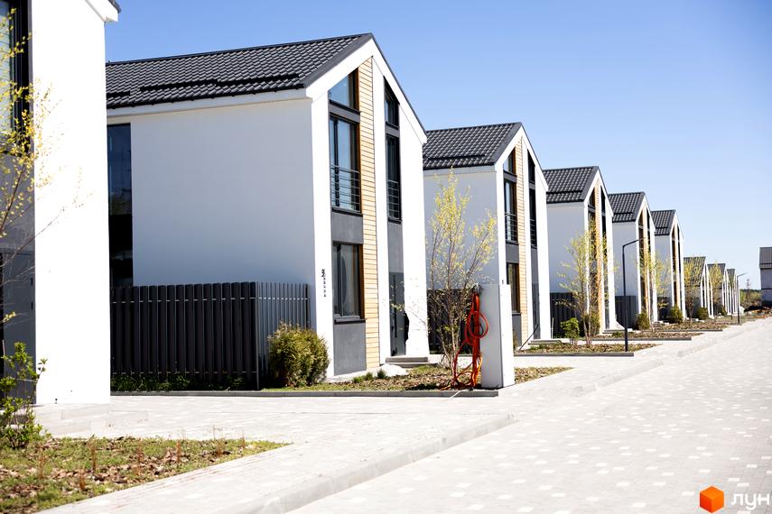 Котеджне містечко Gardd House Eco Village: білі котеджі з темними дахами, великими вікнами та прибудинковою територією з доріжками та деревами.