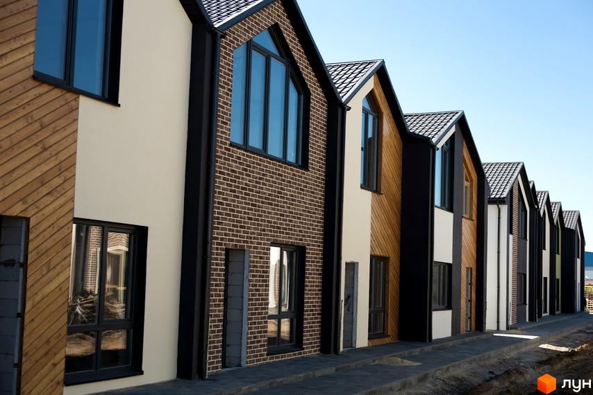 Ряд будинків з різним оздобленням фасадів: дерево, цегла та штукатурка. Бруківка на тротуарі перед будинками.