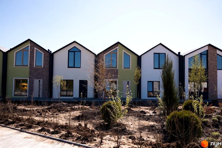 Ряд будинків з білими та зеленими фасадами, чорними дахами та великими вікнами. На передньому плані - рослинність та земля.