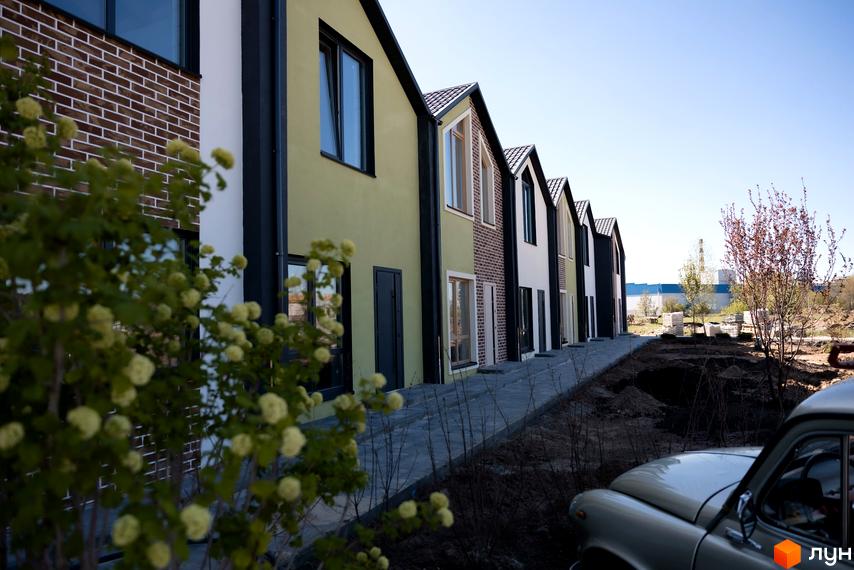 Ряд будинків з фасадами різних кольорів, розташованих в житловому районі. Поруч тротуар та зелені насадження.