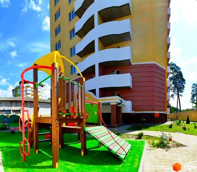 Житловий комплекс Паркова Оселя: жовта багатоповерхівка з білими балконами та дитячим майданчиком на зеленій території.