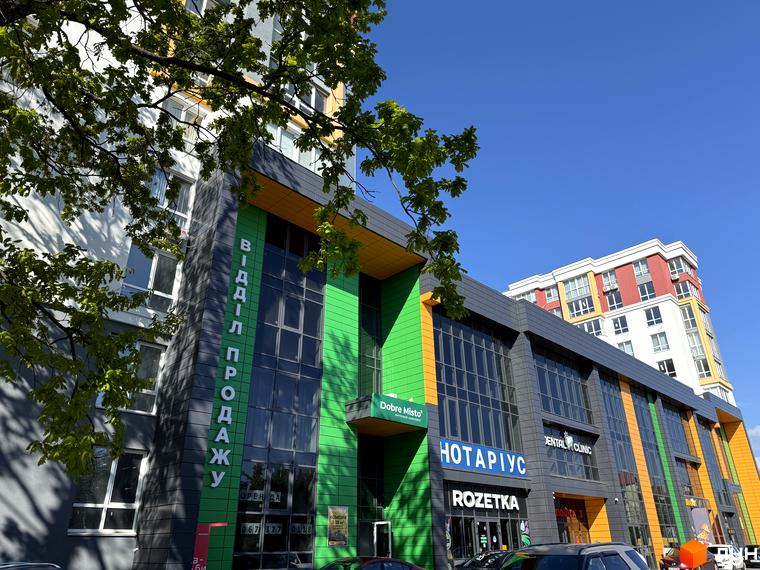 Фасад будівлі з яскравими вставками, де розміщені офіси та магазини, зокрема Rozetka. На стіні великий напис