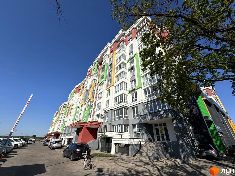Зовнішній вигляд Житлового комплексу Добре Місто 2, багатоповерховий будинок з кольоровими вставками. На передньому плані парковка з автомобілями.