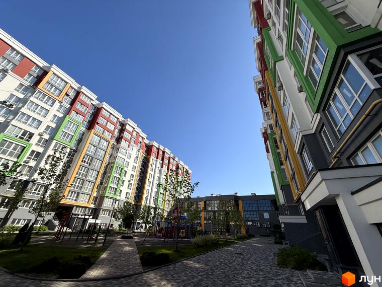 Багатоповерховий будинок ЖК Добре Місто 2 з яскравим фасадом та доглянутою прибудинковою територією з дитячим майданчиком.