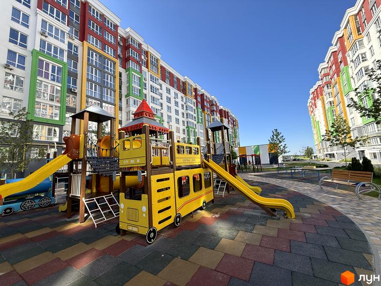 Зображення Житлового комплексу Добре Місто 2 з кольоровими фасадами та дитячим майданчиком у вигляді жовтого автобуса.