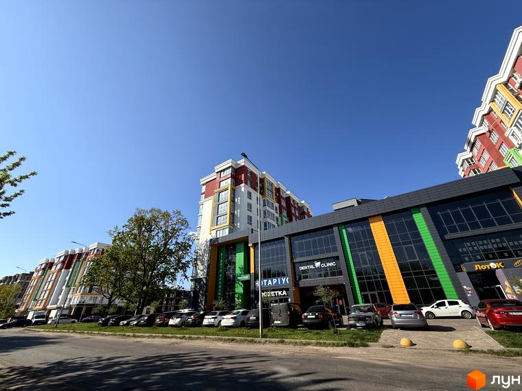 Зображення Житлового комплексу Добре Місто 2. Багатоповерхові будинки з кольоровими фасадами та комерційними приміщеннями, припарковані автомобілі.