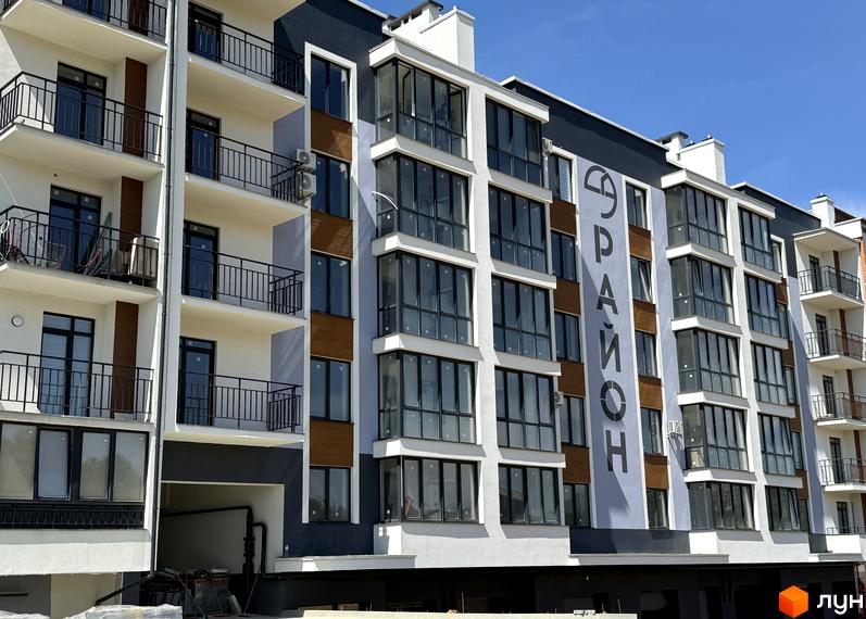 Зовнішній вигляд новобудови ЖК 9 Район з великою кількістю вікон та балконів. Фасад будинку оздоблений сірими та коричневими елементами.