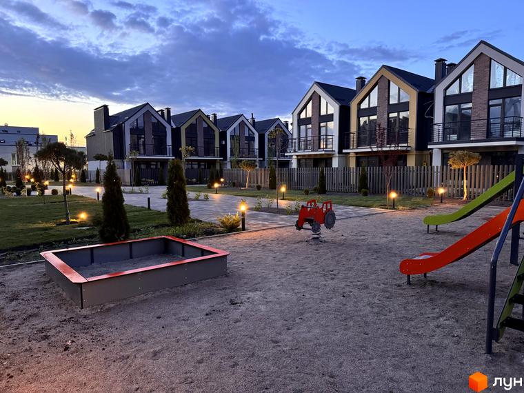 Таунхауси „Петрівське містечко“ з темними дахами та панорамними вікнами. Перед ними дитячий майданчик із гірками та пісочницею.