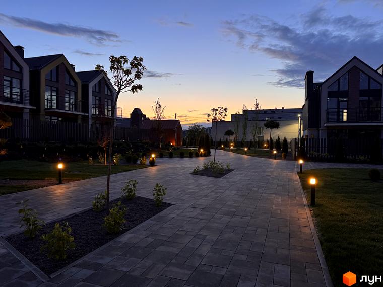 Таунхауси Петрівське містечко. Зовнішній вигляд будинків з великими вікнами та балконами, освітлена бруківка та зелені насадження біля новобудов.