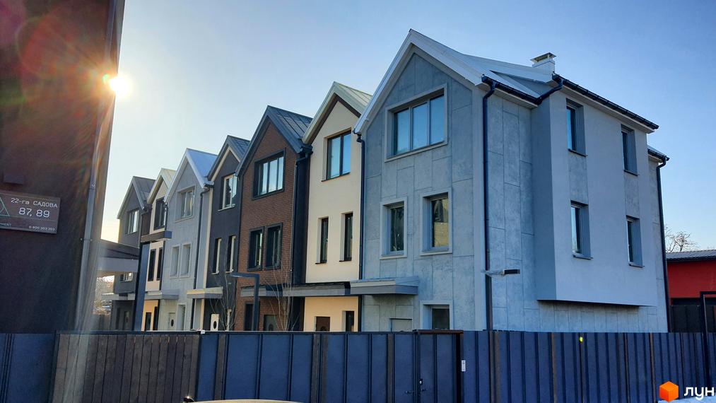 Таунхауси New Smart 12 з сірим фасадом та цегляними елементами, розташовані вздовж паркану під яскравим сонцем.