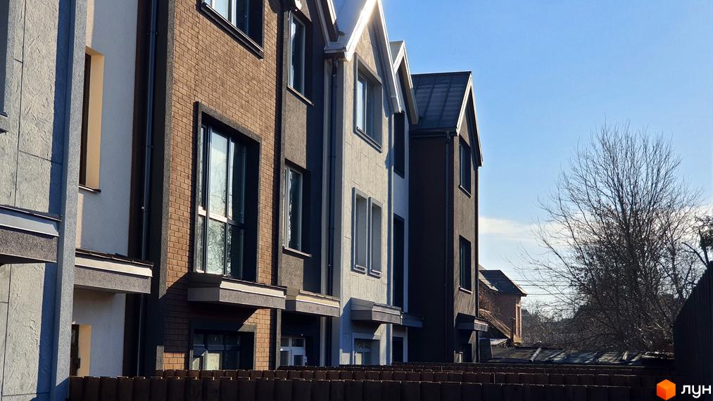 Фасад таунхаусів New Smart 12 з цегляним та штукатурним оздобленням на тлі блакитного неба. На передньому плані паркан та дерева.