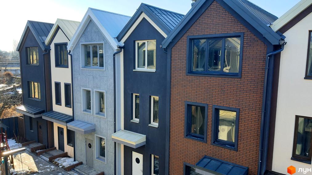 Таунхауси New Smart 12 - це сучасний житловий комплекс з різнокольоровими фасадами та великими вікнами. Перед будинками розташовані доглянуті подвір'я з доріжками та снігом.