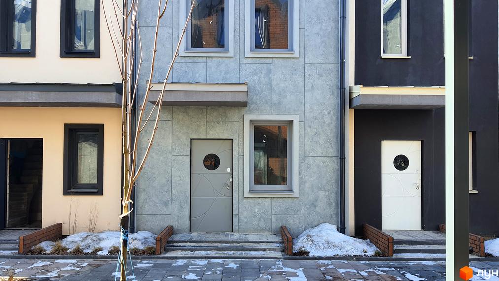 Фасад таунхаусу в Житловому районі New Smart 12 з сірим оздобленням, вікнами та вхідними дверима. Перед будинком тротуарна плитка та сніг.