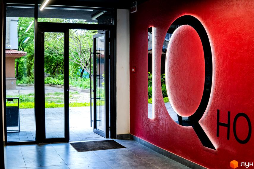 Вхідна група в Житловий комплекс IQ House з логотипом на червоній стіні. Відчинені двері з видом на зелений двір.