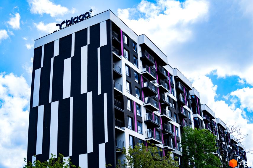 Зображення фасаду ЖК IQ House з балконами на фоні хмарного неба. Вигляд на багатоповерховий будинок з прибудинковою територією.