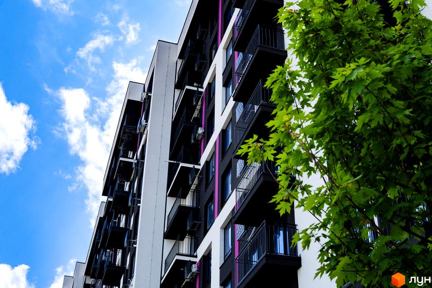 Зображення фасаду новобудови IQ House з балконами на тлі блакитного неба. Поруч зелені дерева.