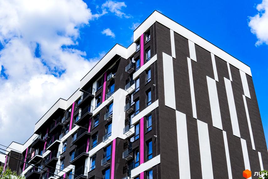 Зовнішній вигляд будинку Житлового комплексу IQ House з балконами та вікнами на фоні блакитного неба з хмарами. Фасад будинку оздоблений в темних та білих кольорах.