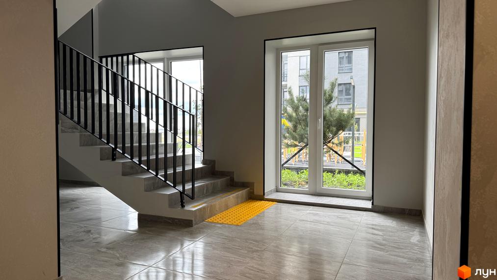 Вхідна група та сходова клітина в житловому комплексі Park Residence з великими вікнами та видом на зелену зону.