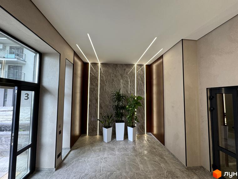 Вхідна група житлового комплексу Park Residence з мармуровим оздобленням та вбудованим освітленням. Дизайн під'їзду з рослинами у білих кашпо.