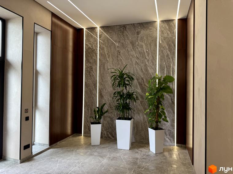 Житловий комплекс Park Residence: сучасний хол з мармуровими стінами та вбудованим освітленням, доповнений зеленими рослинами в білих кашпо.