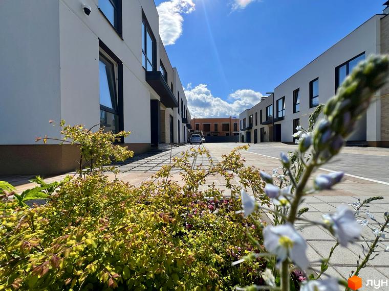 Таунхауси Soul City: білі будинки з темними вікнами та доглянута прибудинкова територія з зеленими насадженнями та квітами.