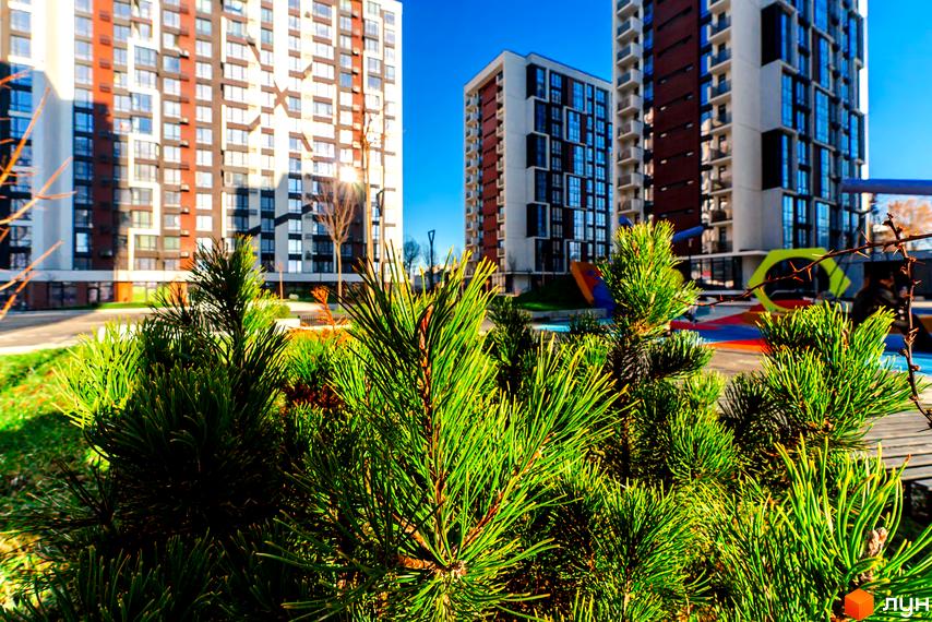 Житловий район Manhattan – сучасні багатоповерхові будинки з панорамними вікнами та облаштована прибудинкова територія з дитячим майданчиком. Зелені насадження та сонячний день.