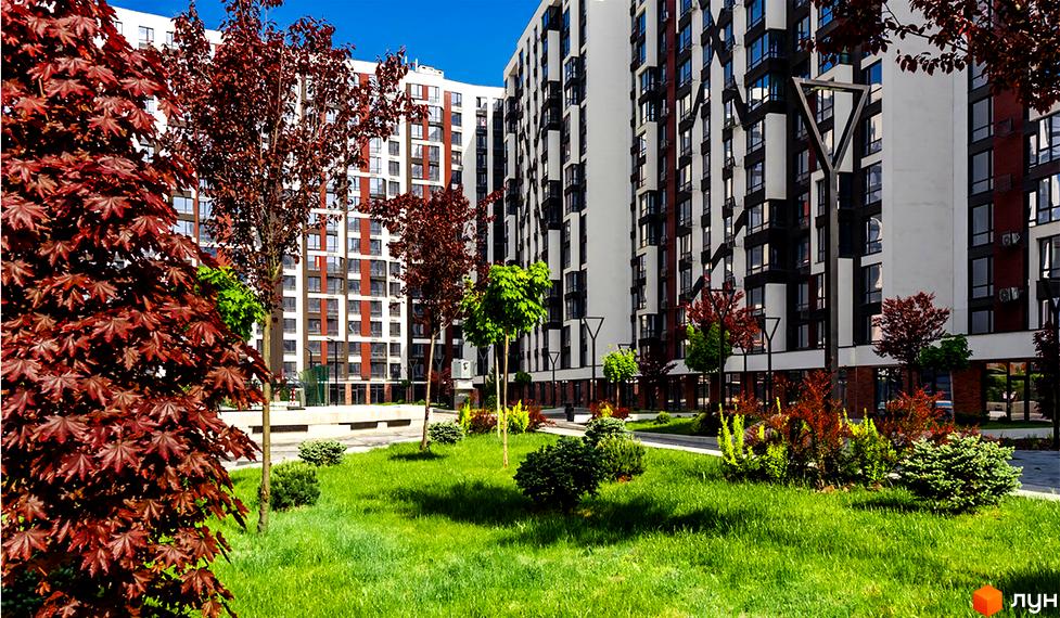 Житловий район Manhattan: фасад новобудови з білими та бордовими елементами, великою кількістю вікон. Прибудинкова територія з доглянутим газоном, деревами та кущами.