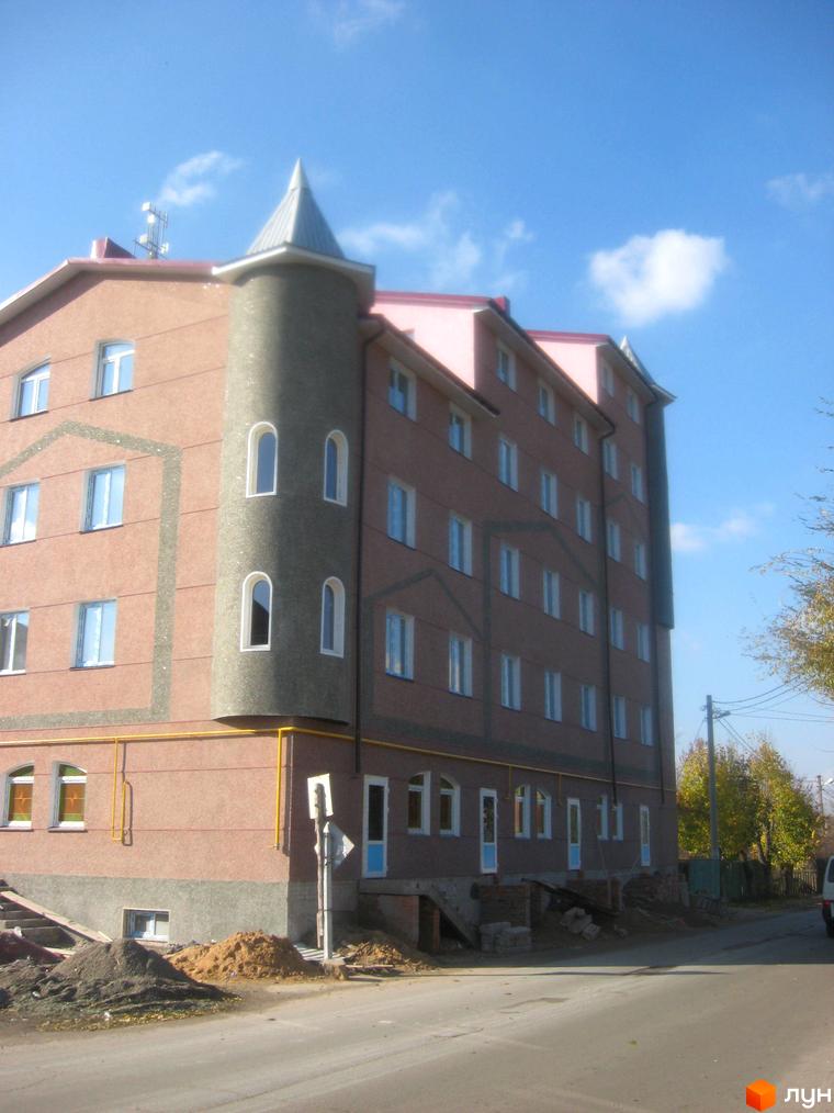 Житловий комплекс Фортеця – багатоповерхова будівля з вежею та рожевим дахом, розташована біля дороги з будівельними матеріалами.