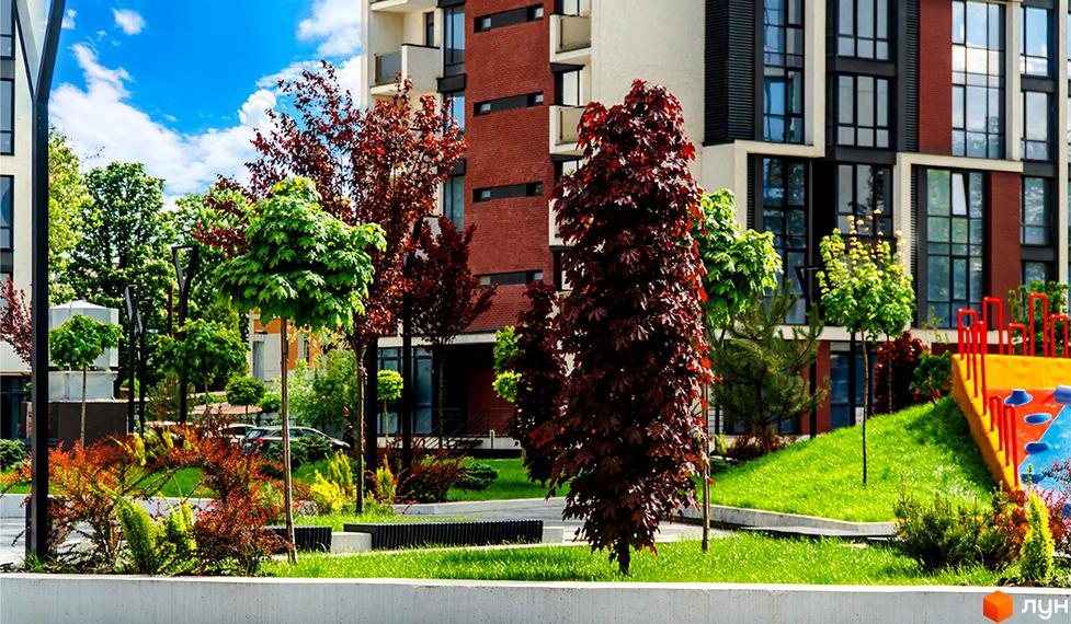 Житловий район Manhattan. Сучасна архітектура будинку з цегляним фасадом та великими вікнами. Доглянута прибудинкова територія з зеленими насадженнями та дитячим майданчиком.