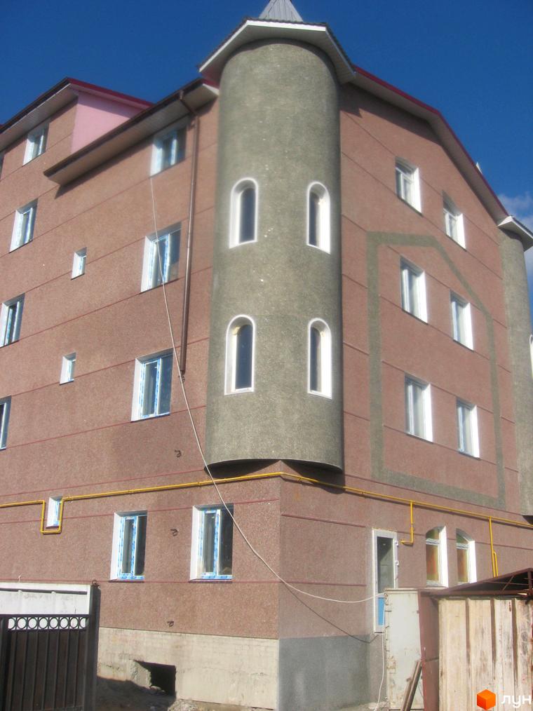 Зовнішній вигляд житлового комплексу Фортеця з круглою вежею та арочними вікнами. Навколо будинку видно елементи прибудинкової території та паркан.