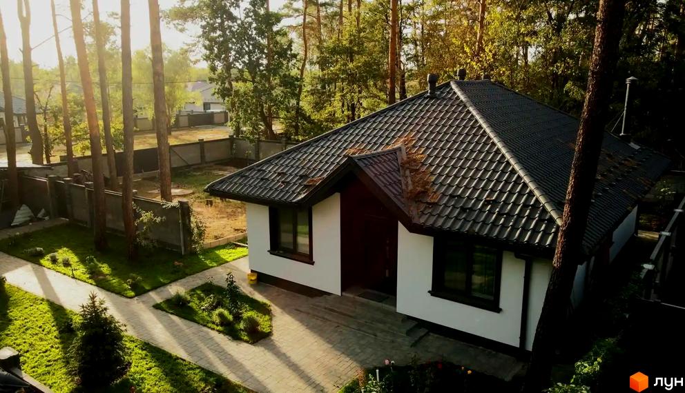 Зображення будинку в Котеджному містечку HED з чорною черепицею на даху та білими стінами. Навколо будинку зелений газон і дерева.