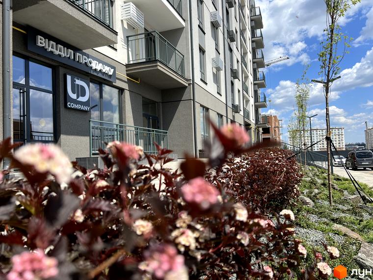 Зовнішній вигляд новобудови ЖК Park Residence з фасадом сірого кольору та балконами. На прибудинковій території висаджені кущі з рожевими квітами та дерева.