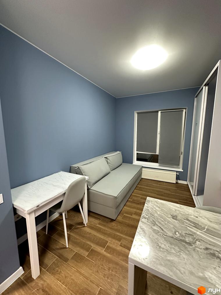 Затишна кімната з диваном та столом у ЖК Комфортне містечко. Сірі стіни та дерев'яна підлога створюють спокійну атмосферу.