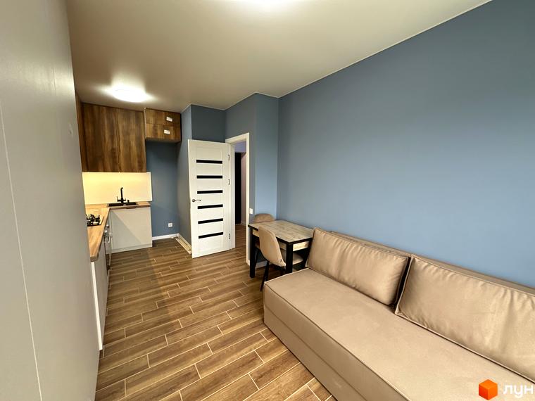 Житловий комплекс Комфортне містечко: світла вітальня з диваном та кухня з дерев'яними фасадами.