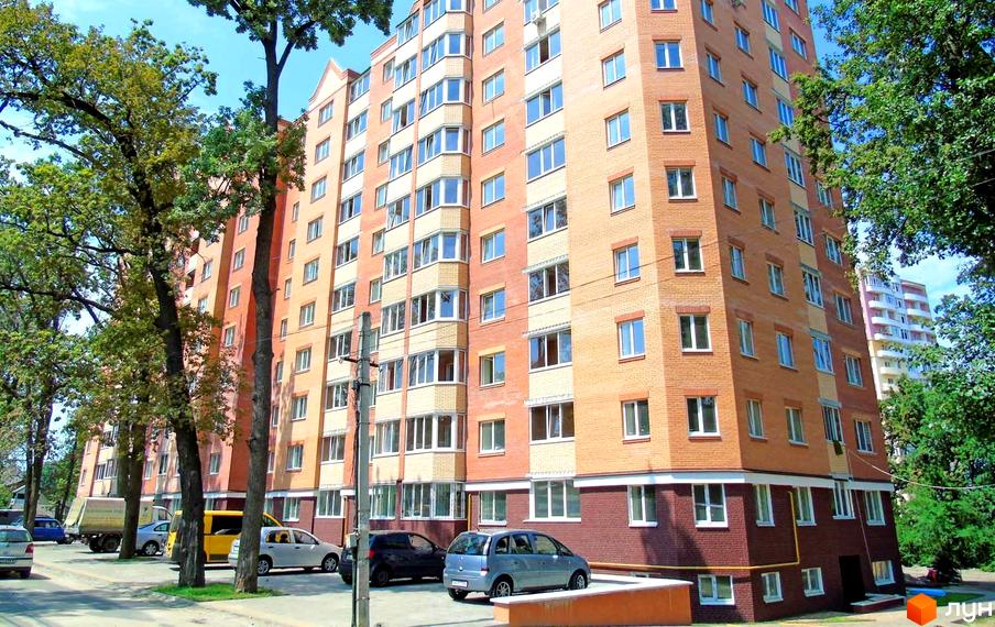 Зовнішній вигляд цегляної новобудови ЖК Столичний квартал з численними вікнами та балконами. Навколо будинку розташовані дерева та припарковані автомобілі.