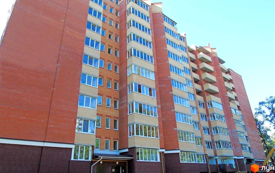 Житловий комплекс Столичний квартал: висотна будівля з червоної цегли та світлими елементами фасаду, великою кількістю вікон і балконів. Ясне небо.