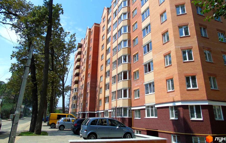 Зовнішній вигляд цегляної новобудови ЖК Столичний квартал з балконами та вікнами. Поруч розташовані дерева та припарковані автомобілі.