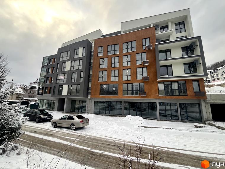 Зимовий вигляд ЖК Forest Residence Polyana. Багатоповерховий будинок з панорамними вікнами та комерційними приміщеннями на першому поверсі, навколо сніг.