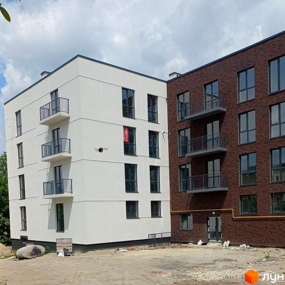 Житловий комплекс на вул. Стадникової, 40: завершені білий та цегляний будинки з балконами. Прибудинкова територія з ґрунтовим покриттям.