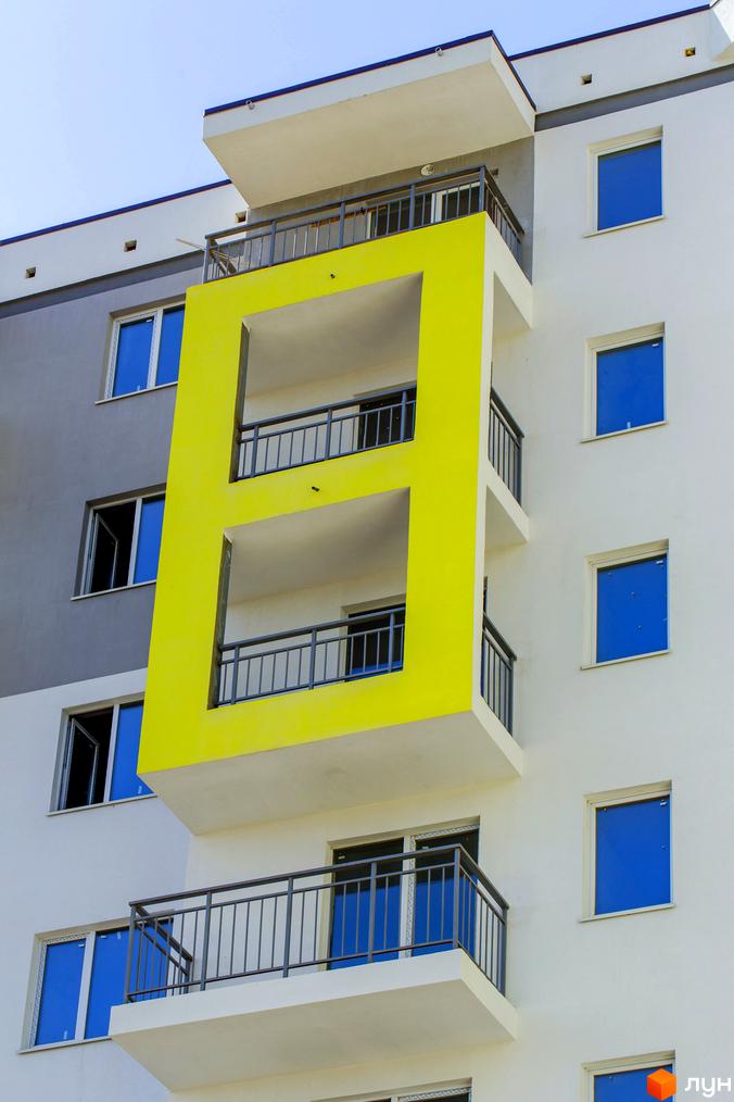 Фасад житлового комплексу ЖК Сан Сіті з яскравим жовтим елементом та синіми вікнами. Будинок має балкони з металевими огорожами.