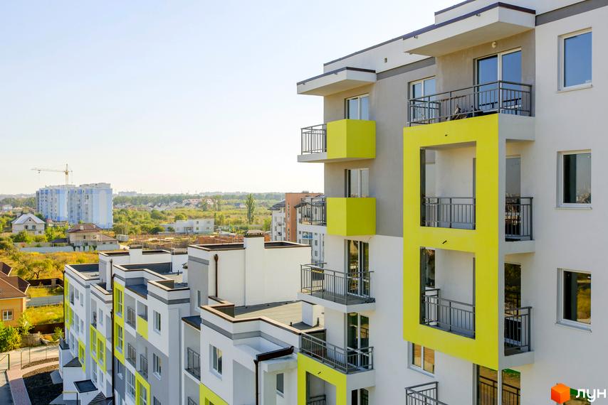 Зовнішній вигляд новобудови ЖК Сан Сіті з яскравими жовтими елементами та балконами. На тлі видно інші будинки та зелену зону.