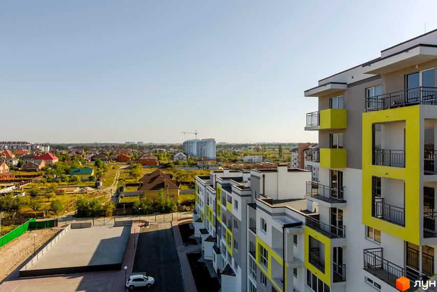 Житловий комплекс Сан Сіті: багатоповерхівка з жовтими акцентами на фасаді та відкритими балконами. Прибудинкова територія з дорогою та зеленню.