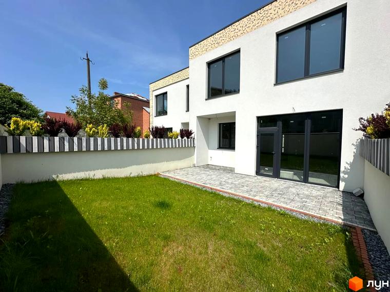 Зовнішній вигляд двоповерхового будинку з великими вікнами та терасою. Прибудинкова територія з газоном та огорожею.